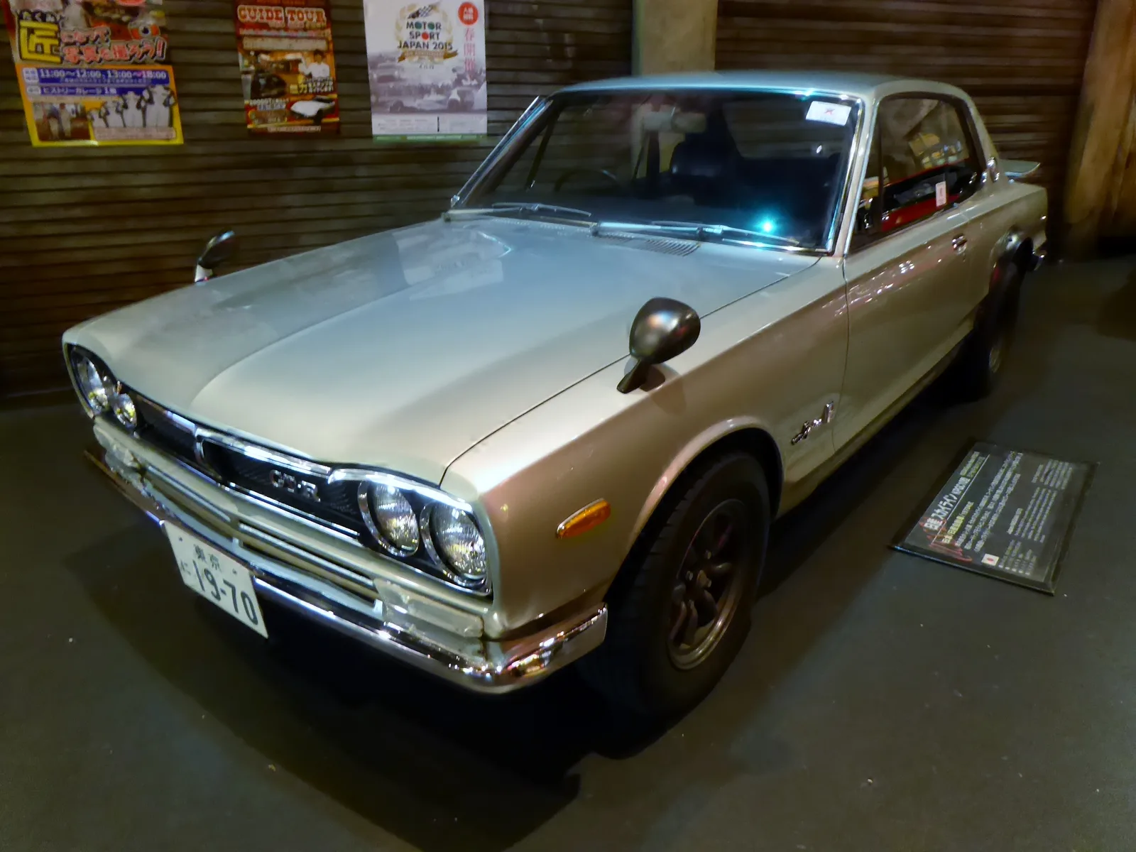 Nissan Skyline 2000GT-R (Hakosuka) สีทองแชมเปญ มุมหน้าเฉียงในพิพิธภัณฑ์แสงหม่น