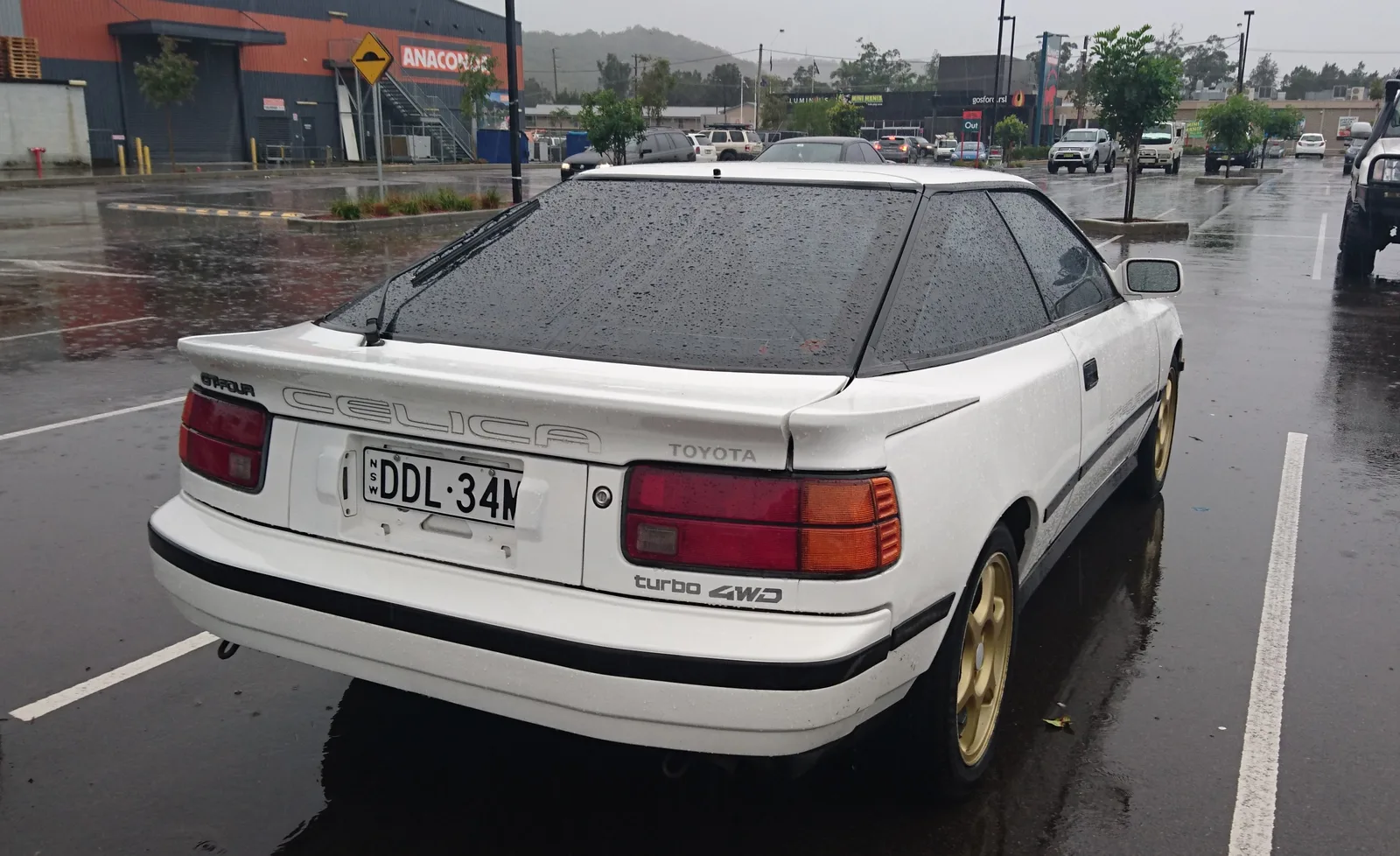 Celica GT-Four สีขาวล้อ BBS ทอง มุมท้ายสามส่วนท่ามกลางสายฝน