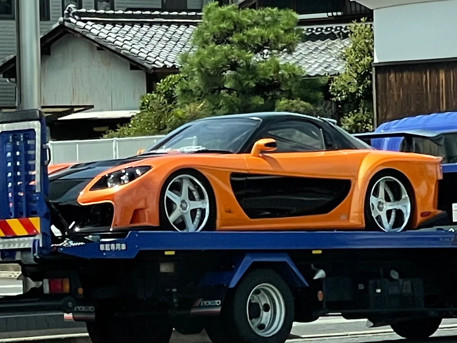 Fortune RX-7 สีส้มบนรถลาก จอดหน้าบ้านไม้ญี่ปุ่นหลังคากระเบื้อง บรรยากาศถนนจริง