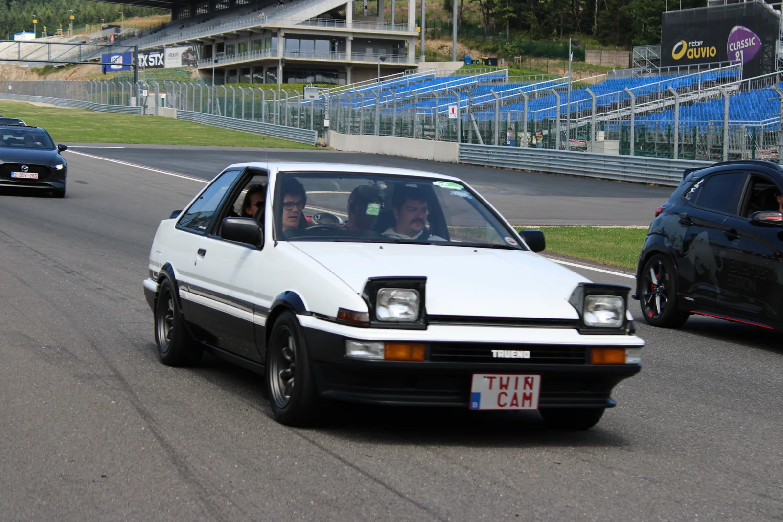 โตโยต้า AE86 เทรโน ขาวคาดดำ กำลังวิ่งบนสนามแข่ง มุมหน้าสามส่วน บรรยากาศเรซซิ่ง