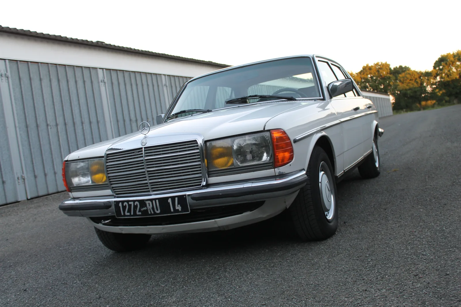W123 280E สีขาว มุมหน้าเฉียงต่ำหน้าโรงรถยามเย็น ให้ฟีลคลาสสิกหรูนิ่ง