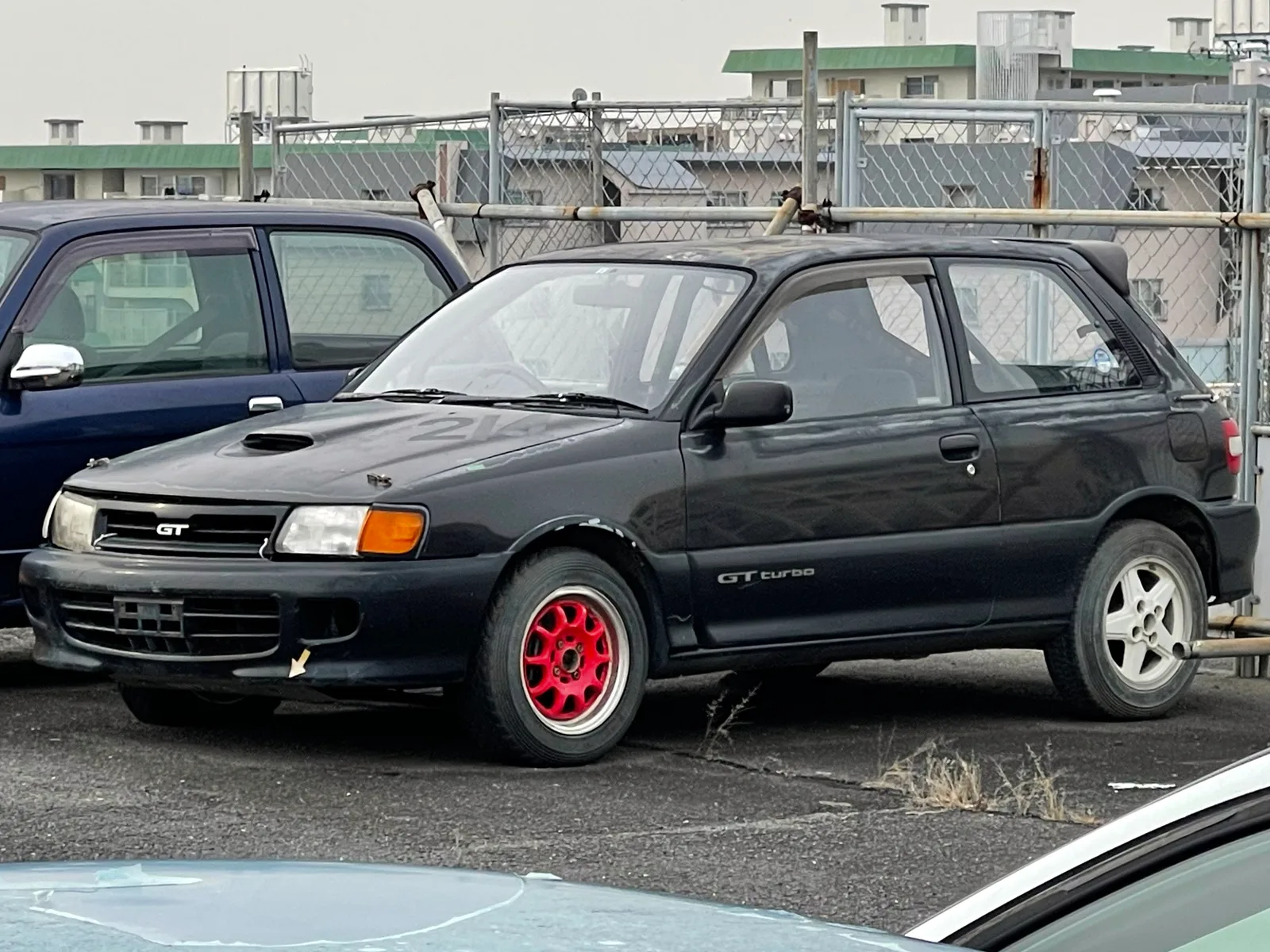 EP82 GT Turbo สีดำ แต่งล้อแม็กแดง จอดในลานจอดย่านที่พักอาศัยญี่ปุ่น มุมหน้าสามส่วน