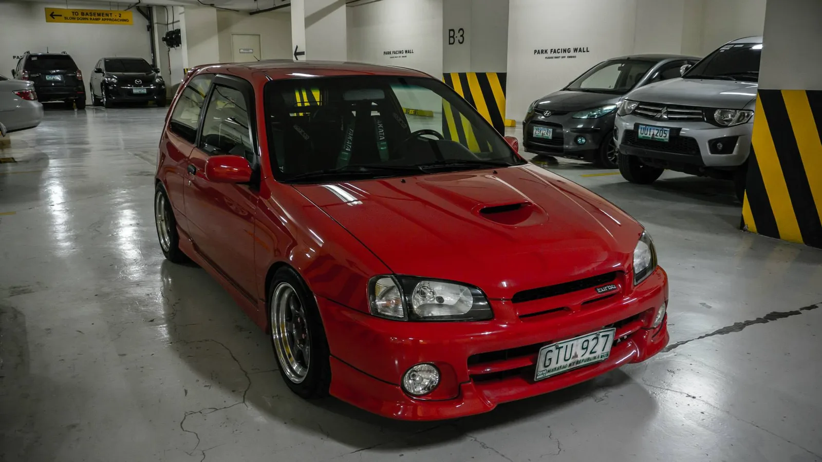 Glanza V สีแดง แต่งเรซซิ่งมีโรลเคจในห้องโดยสาร จอดในลานจอดรถ ฟิลิปปินส์