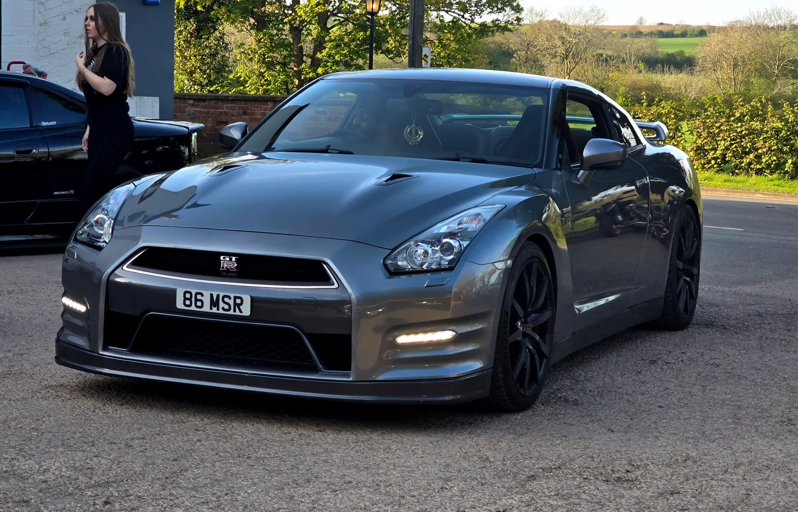 GT-R R35 สีเทาเข้ม มุมหน้าเฉียงสามส่วน จอดริมถนนชนบทประเทศอังกฤษ