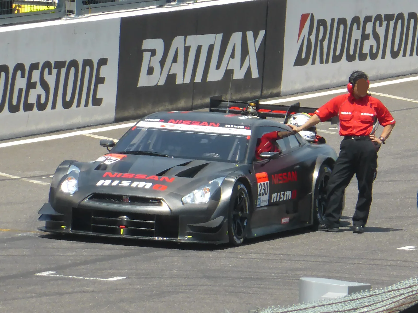 GT-R (R35) Super GT ทีม NISMO สีเทาดำ จอดพิตเลน มีทีมงานยืนประกบข้างรถ บรรยากาศสนามจริง
