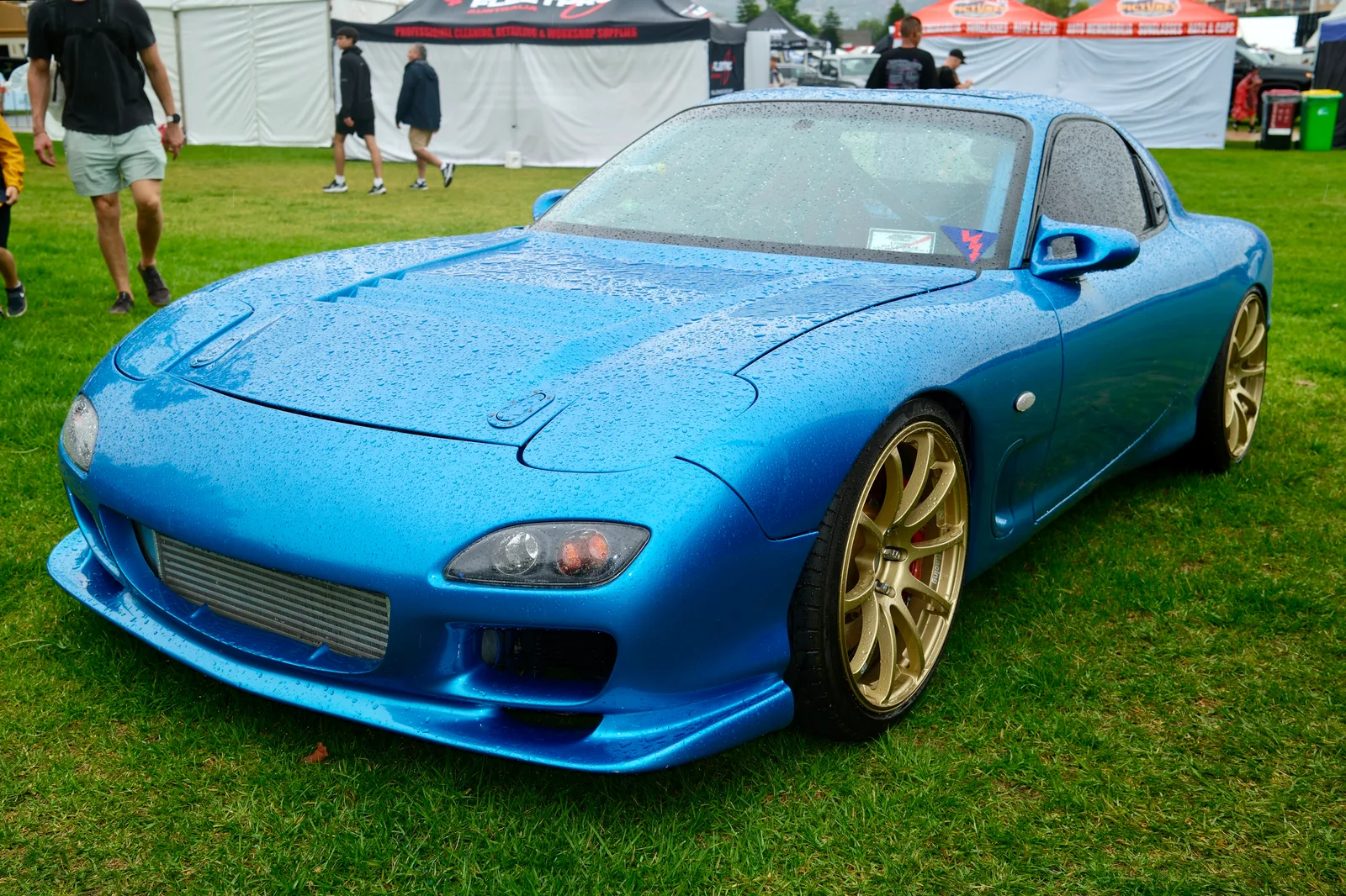 Mazda RX-7 FD3S สีฟ้า มุมหน้า 3/4 กลางงานรวมรถบนสนามหญ้า