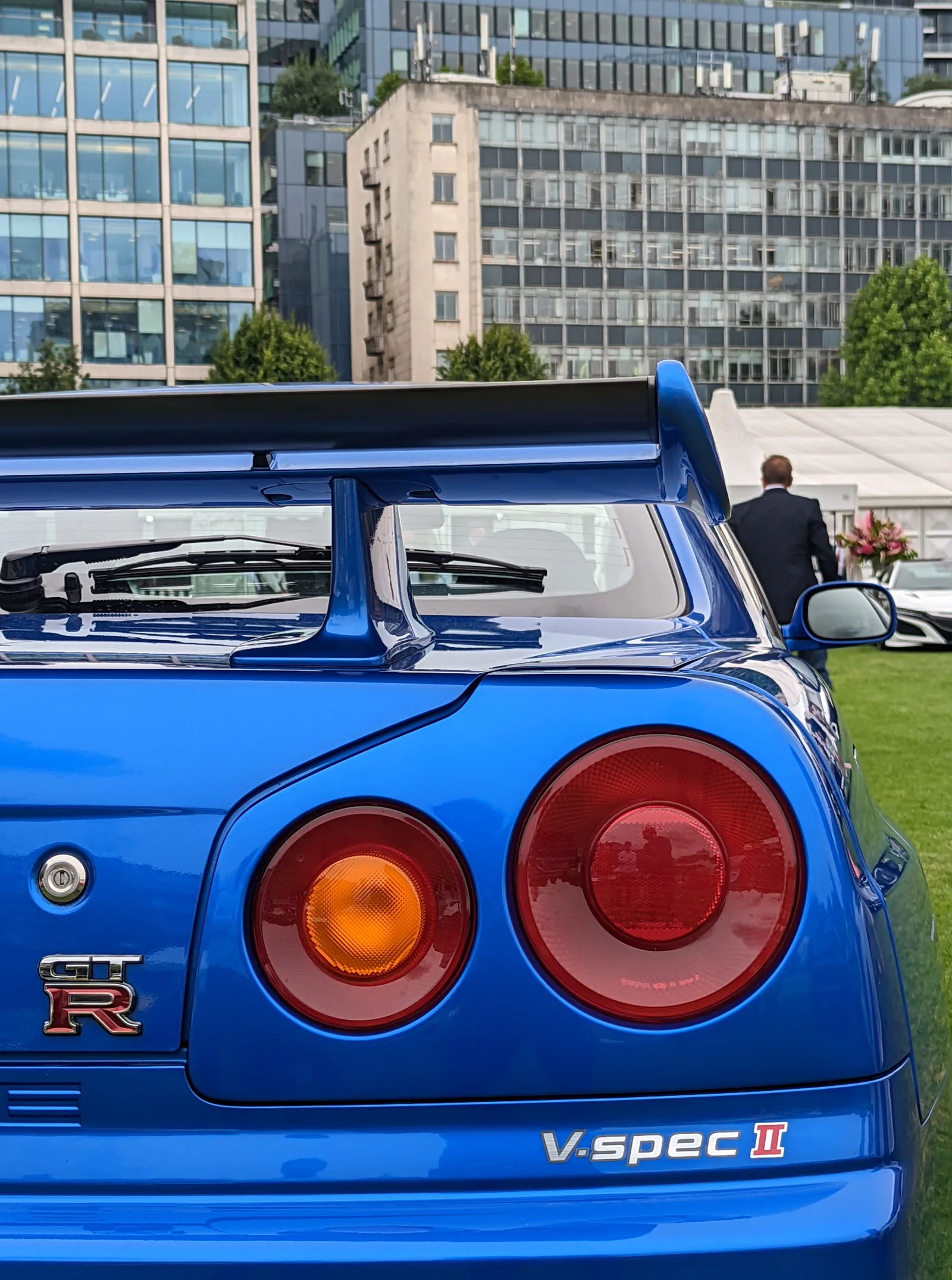 ดีเทลไฟท้าย GT-R R34 V-spec II สีน้ำเงิน ปีกหลังคาร์บอน ฉากหลังตึกสูงใจกลางเมือง