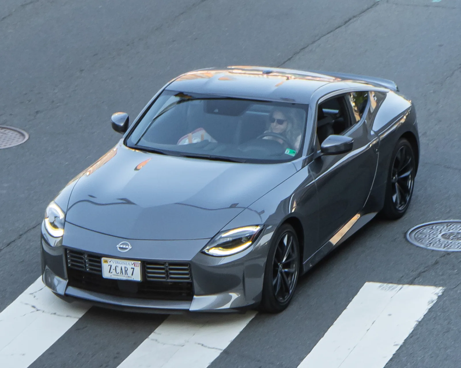 Fairlady Z รุ่นมาตรฐาน สีเทา วิ่งข้ามทางม้าลายกลางเมือง มุมเงยแบบไดนามิกบนถนนจริง