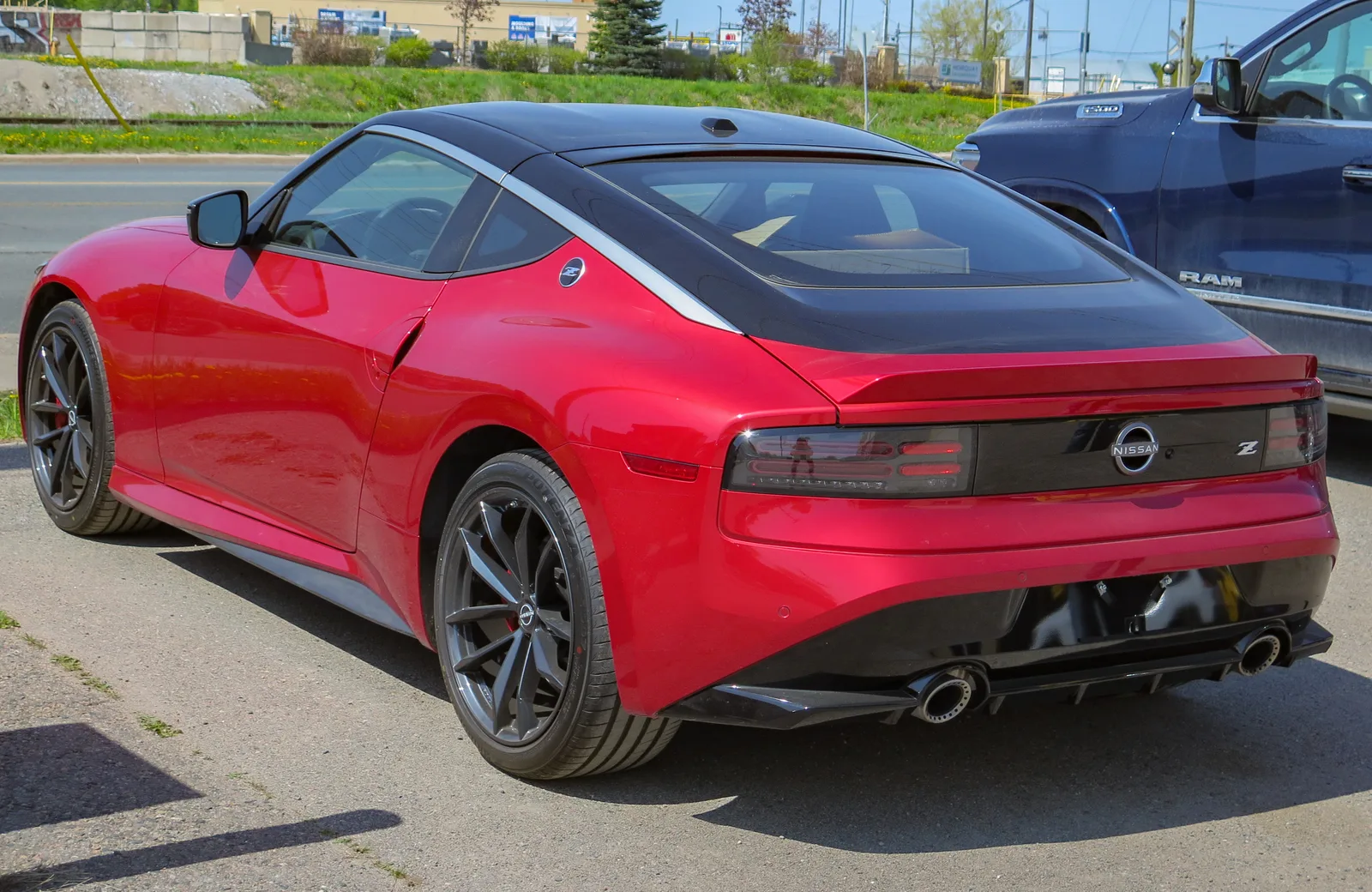 Nissan Z สีแดงมุมท้ายเฉียง จอดในลานกลางแจ้ง โชว์ไฟท้ายทรงเรียวยาว