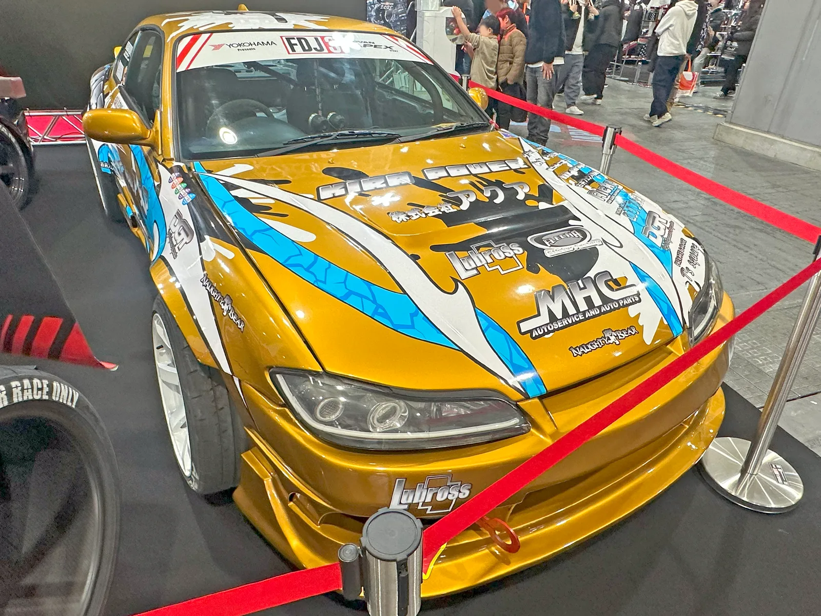Nissan Silvia S15 สีทองลายกราฟิก ทีม FDJ ในบูธโชว์รถ มุมหน้าสามส่วนโชว์ไลน์ตัวถัง