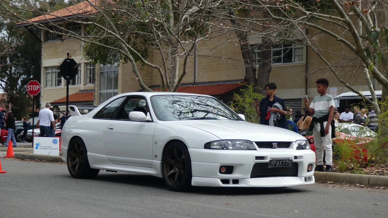 Nissan Skyline GT-R R33 สีขาว ล้อทองแดง มุมหน้าสามส่วนกลางลานจอดงานรวมรถ