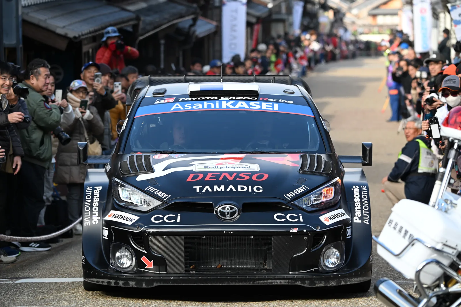 GR Yaris Rally1 คันสีดำชมพูของทีม Toyota Gazoo Racing วิ่งผ่านฝูงชนในสนามแรลลี่ญี่ปุ่น