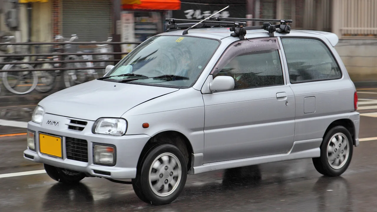 มิระ L500 สีเงินติดแร็คหลังคา วิ่งบนถนนญี่ปุ่นวันฝนตก ตัวถังทรงมนของเจนนี้เห็นชัด