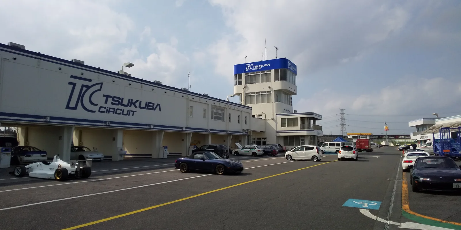 บรรยากาศพิทเลนสนามสึคุบะ มีมาสด้าโรดสเตอร์เปิดประทุนและรถฟอร์มูล่าจอดหน้าอาคาร TSUKUBA CIR
