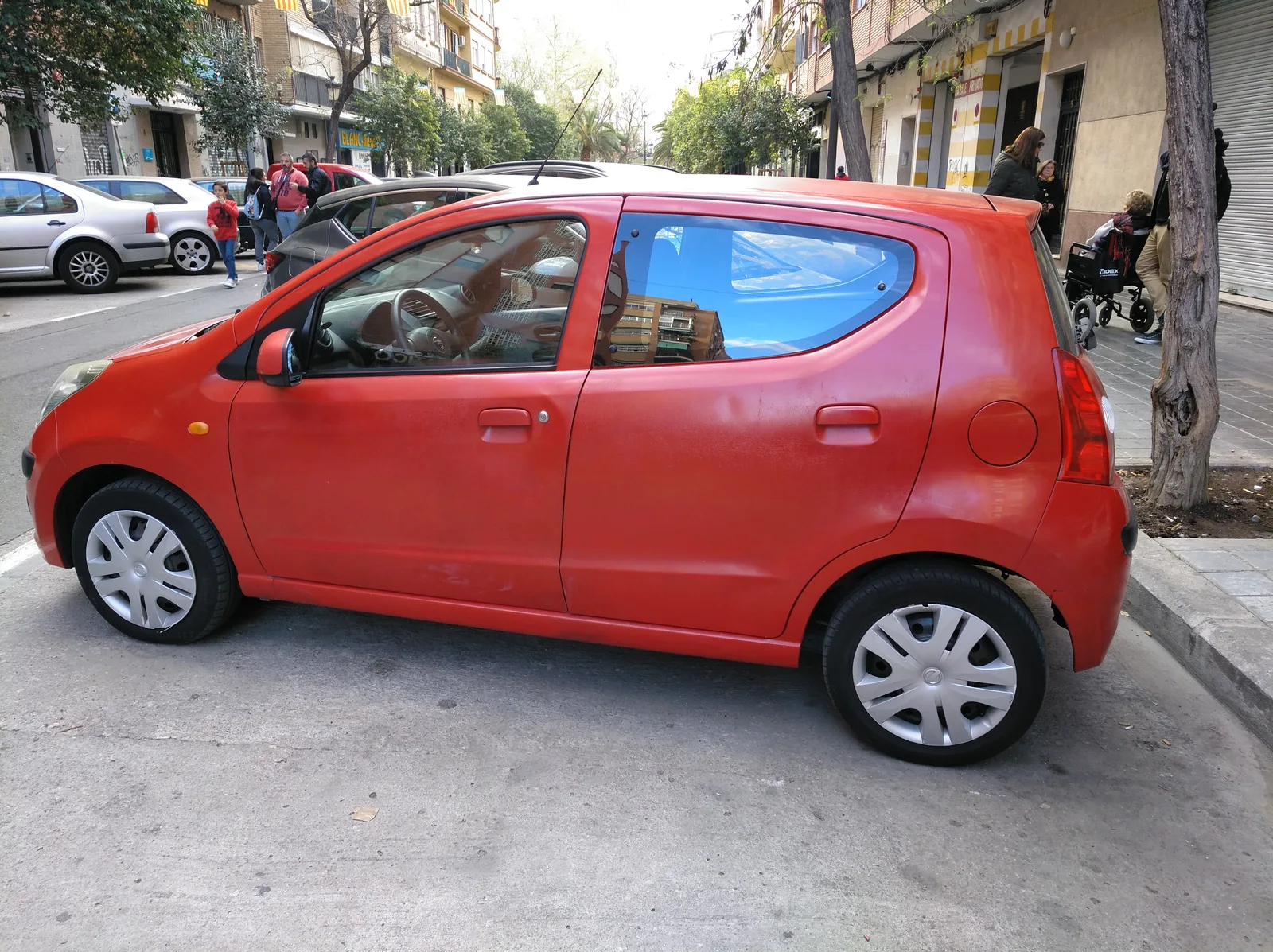 Nissan Pixo รุ่นเก่า สีส้มแดง มุมข้าง จอดริมถนนในสเปน สะท้อนความจิ๋วของซิตี้คาร์