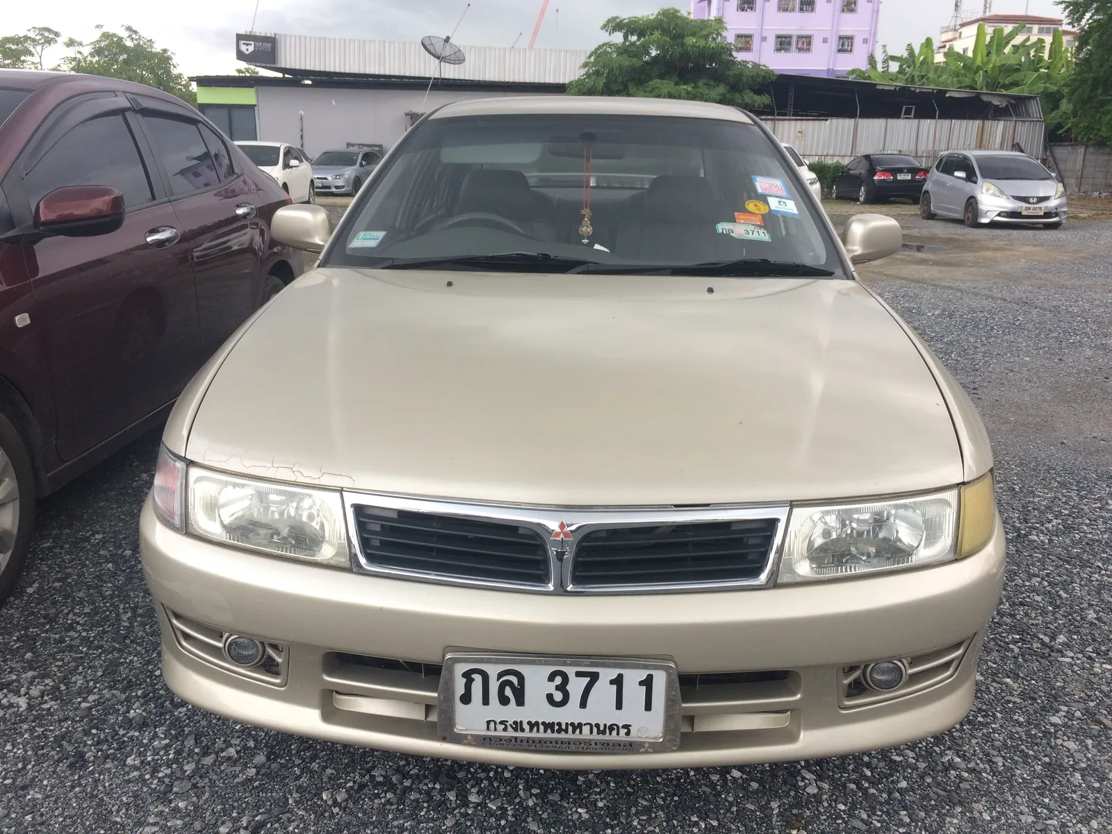 Lancer ท้ายเบนซ์ สีทอง มุมตรงด้านหน้า เห็นกระจังโครเมียม ไฟหน้า และชุดไฟตัดหมอก