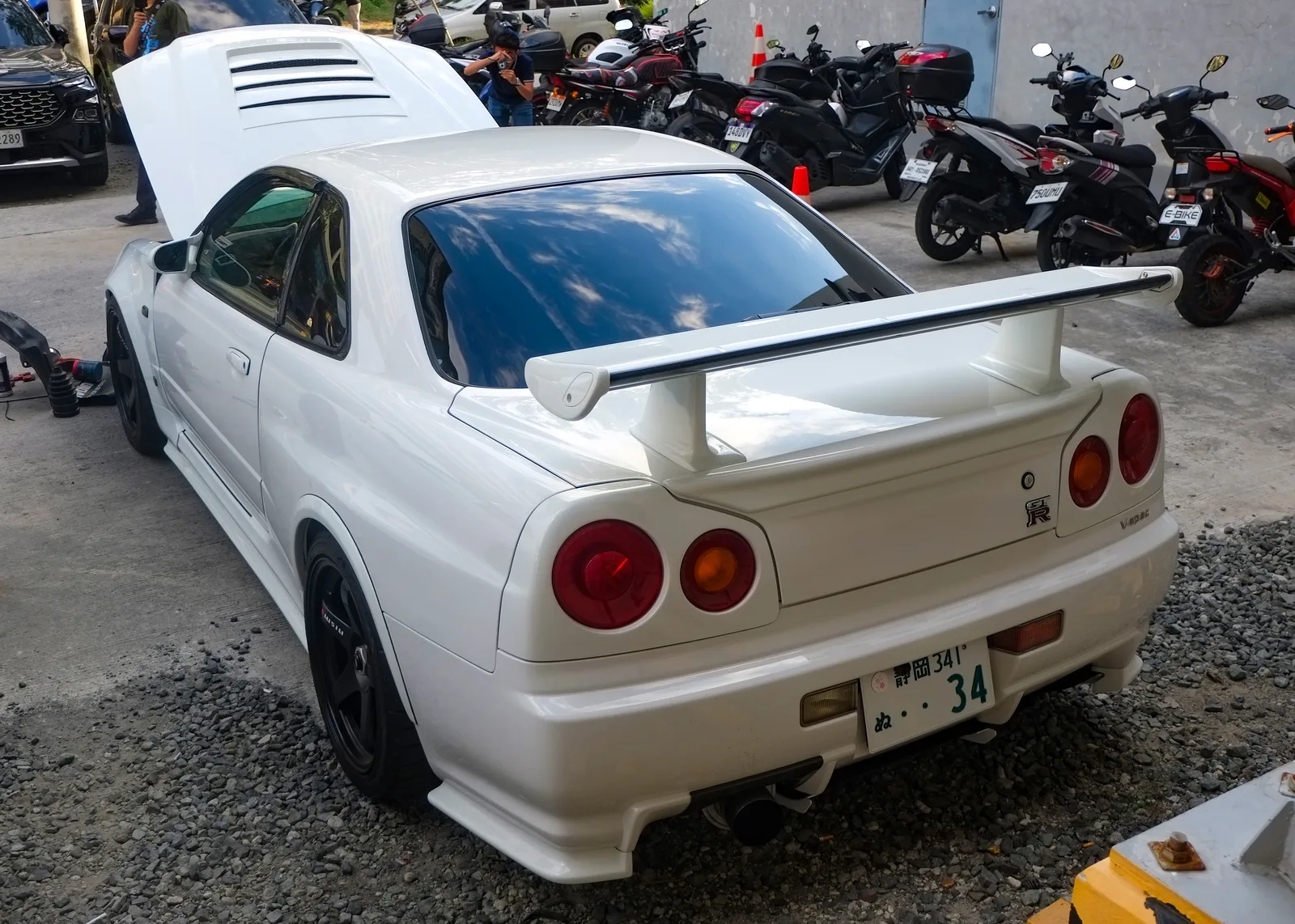 Skyline GT-R R34 V-Spec สีขาว มุมท้ายสามส่วน เห็นไฟท้ายกลมและสปอยเลอร์