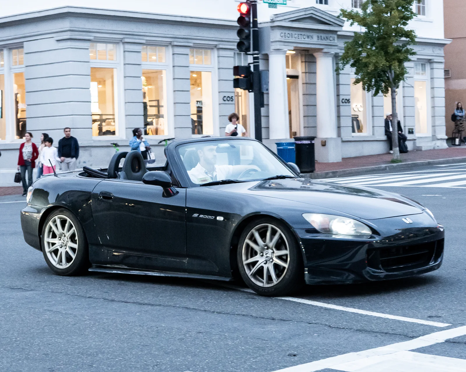 S2000 สีดำเปิดประทุนวิ่งผ่านสี่แยกในเมือง มองจากด้านข้าง