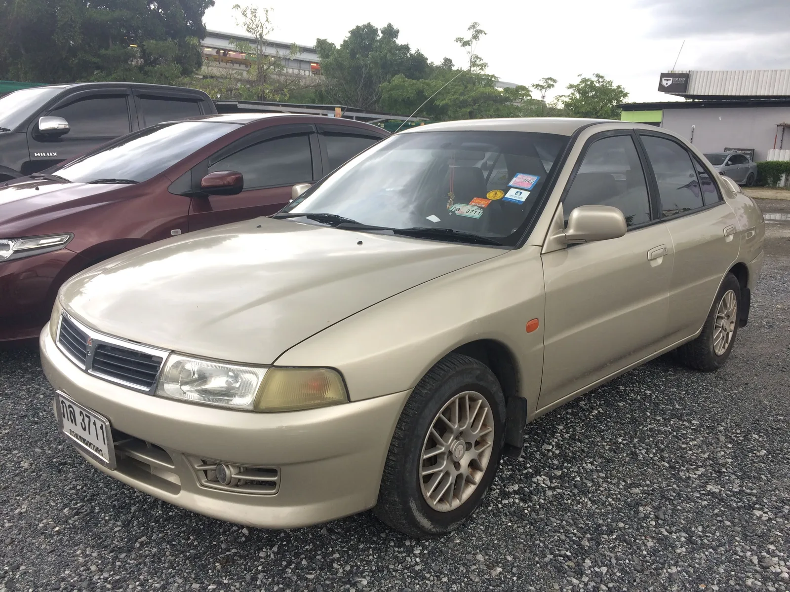 Lancer ท้ายเบนซ์ สีทองแชมเปญ มุมหน้าสามส่วน ไฟหน้าและกระจังหน้าทรงเดียวกับที่คุ้นตาบนถนนไท