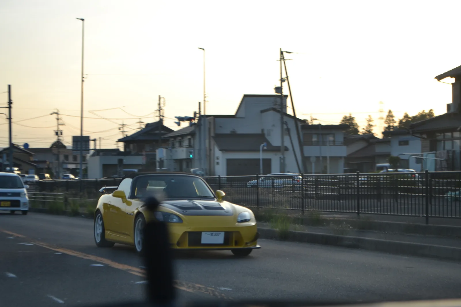 Honda S2000 สีเหลืองวิ่งบนถนนญี่ปุ่นช่วงเย็น ฝากระโปรงดำ มุมหน้าขณะเคลื่อนที่