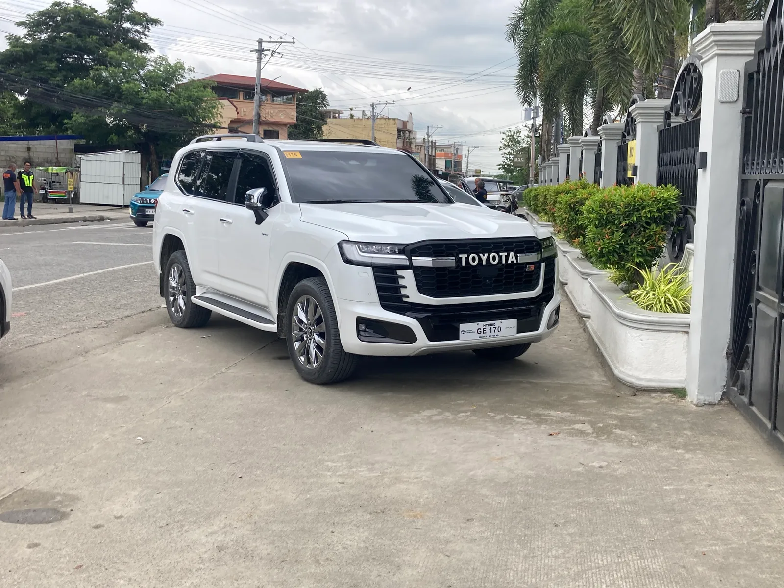 Land Cruiser 300 สีขาว รุ่น GR Sport มุมหน้าสามส่วน ป้ายไฮบริด จอดริมถนนจริง