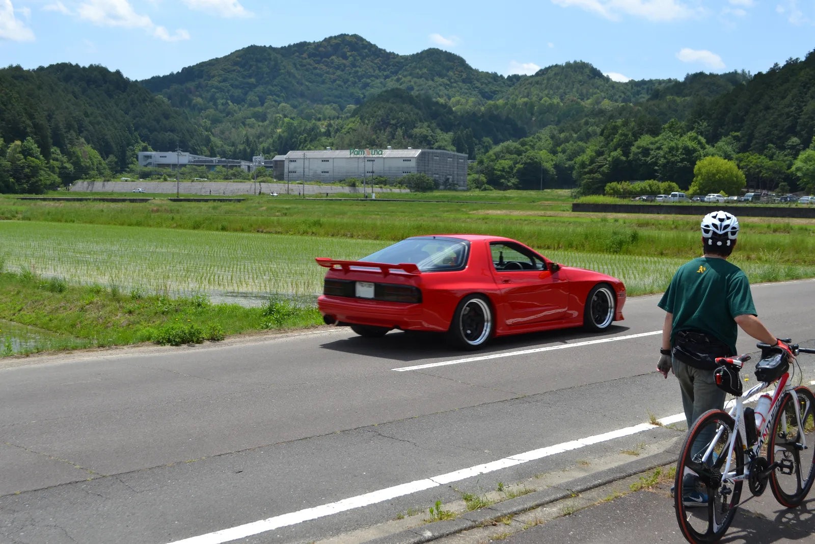 RX-7 FC3S สีแดงวิ่งบนถนนชนบทญี่ปุ่น มองจากด้านท้ายพร้อมปีกหลัง